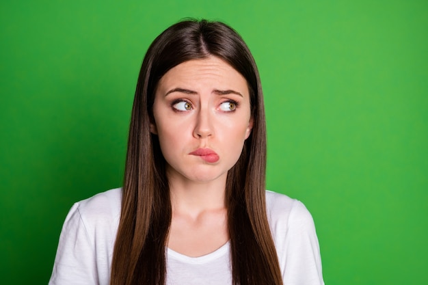 Fotoportret van verwarde vrouw die naar kant kijkt die op levendige groen gekleurde achtergrond wordt geïsoleerd