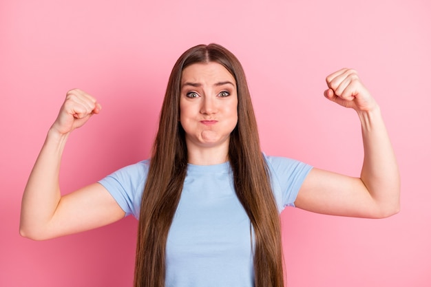 Fotoportret van worstelend meisje met bladerdeegwangen die biceps laten zien buigen geïsoleerd op pastelroze gekleurde achtergrond