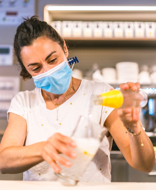 Fotosessie met een serveerster met een gezichtsmasker in een bar. Een frisdrank maken met ijs