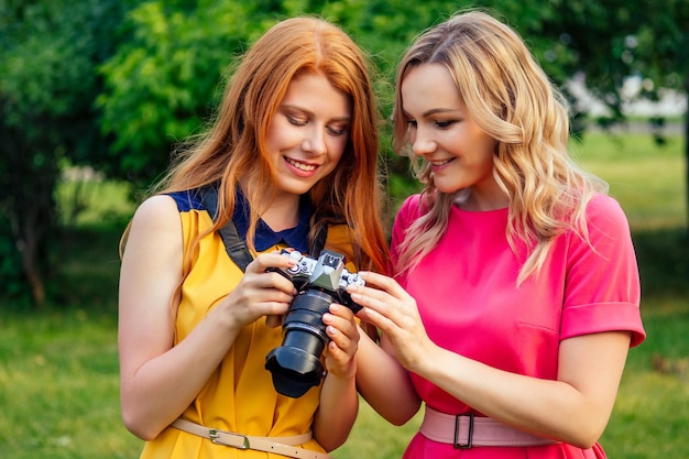 Fotosessie mooie jonge gember roodharige Iers meisje in een gele jurk en Europese blonde vrouw in roze jurk fotografeerden elkaar in het zomerpark fotoshoot van twee model vriendinnen