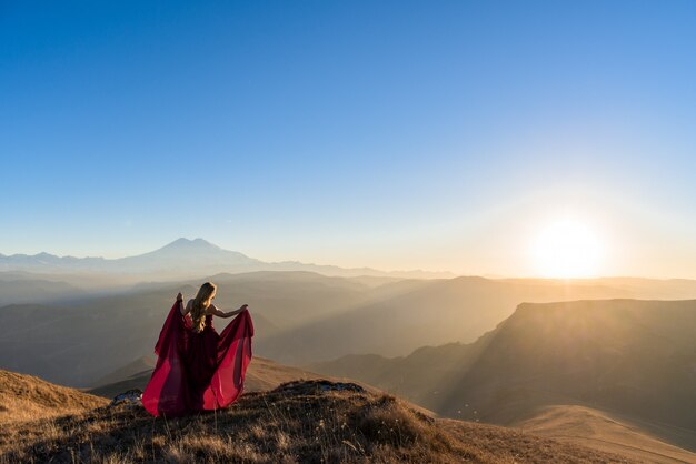 Fotoshoot in de bergen. meisje in een jurk tegen de bergen. tijdens zonsondergang