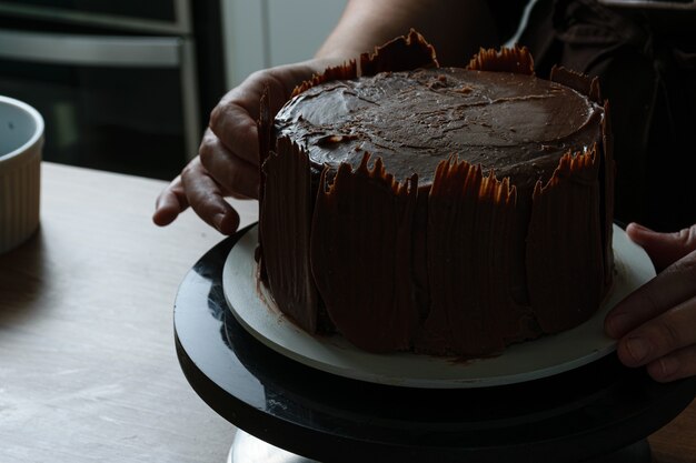 Fotoshoot met chocoladetaart die wordt versierd. Chocoladetaart bedekt met aardbeien, verse basilicumblaadjes, bramenjam en chocoladeplaten rondom.