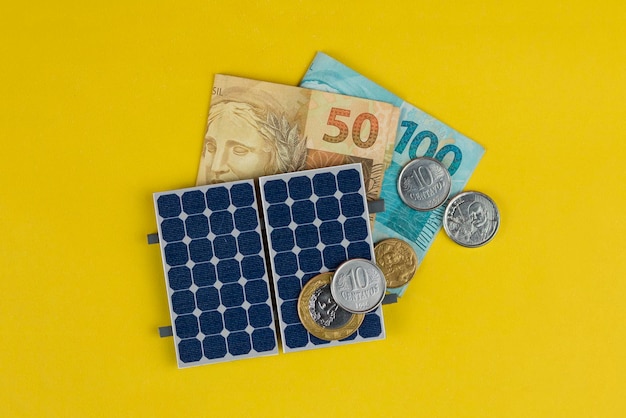 Fotovoltaïsch paneel geld en plug draad geïsoleerd op gele achtergrond olar paneel met gevarieerde waarden van Braziliaans geld alternatieve schone energie bedrijfsconcept