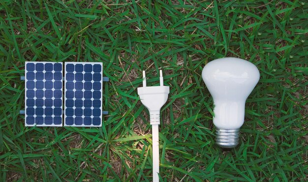 Fotovoltaïsche zonnepaneel lamp plug draad en mobiel op groen gras achtergrond Alternatief schoon en hernieuwbare energie concept