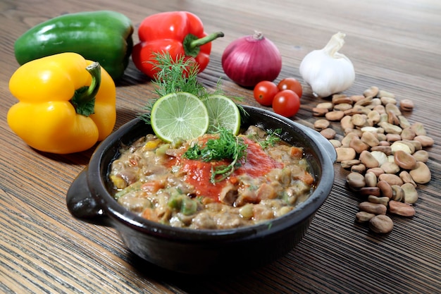 Photo foul beans or faba beans with bell pepper onion garlic cherry tomato served in dish isolated on wooden table side view of arabic food