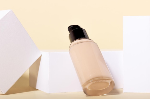 Foundation in a glass bottle on a background of geometric shapes Facial corrector on a beige background with copy space Packaging mockup with copy space