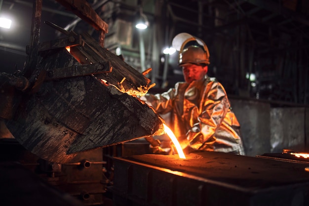 Foundry hardworking people pouring hot liquid iron from bucket into molds, iron ore production and metallurgy.