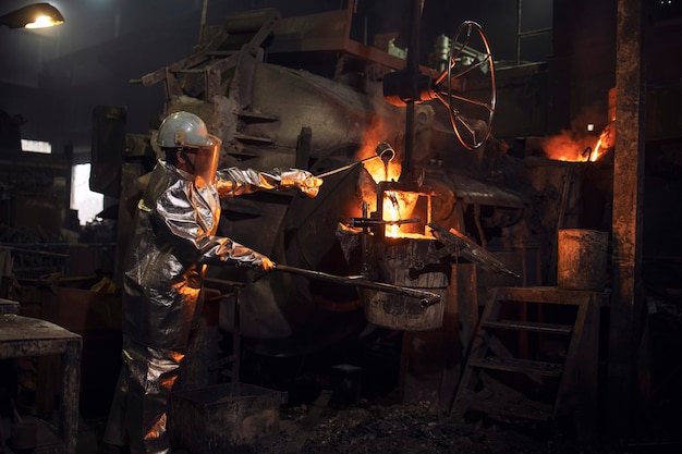 Foundry worker checking molten steel in burning furnace.