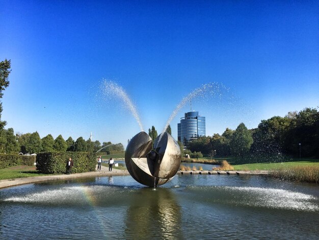 Fountain in lake against clear blue sky