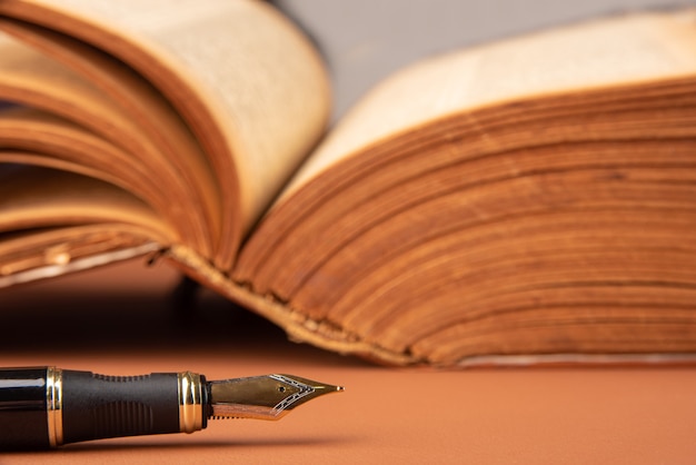 Photo fountain pen, beautiful details of a beautiful fountain pen and an antique book placed on caramel leather, selective focus.