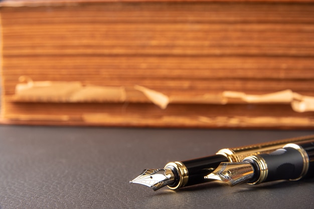 Fountain pen, beautiful details of two beautiful fountain pens and an antique book placed on black leather, selective focus.