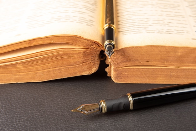 Fountain pen, beautiful details of two beautiful fountain pens and an antique book placed on black leather, selective focus.