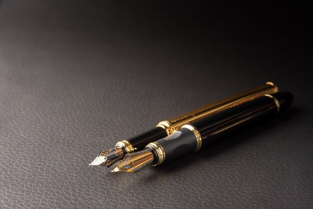 Fountain pen, beautiful details of two beautiful fountain pens placed on black leather, selective focus.