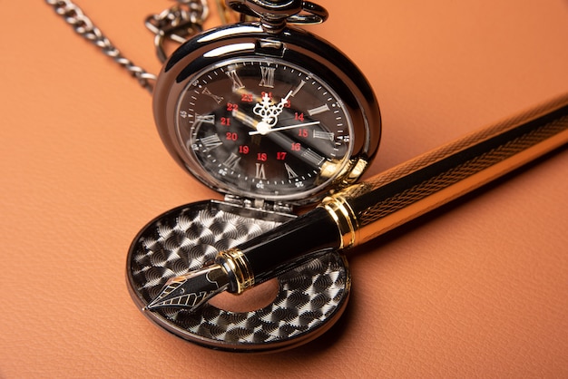 만년필과 시계, 만년필의 아름다운 세부 사항과 가죽 표면에 노출된 골동품 시계, 선택적 초점.