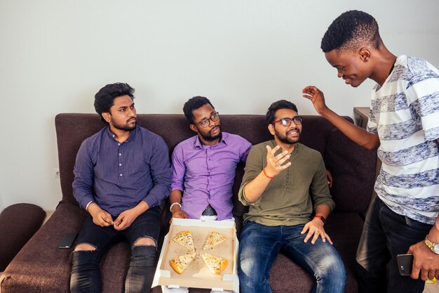 4명의 아프리카계 미국인 남성이 홈 파티에서 피자를 먹고 악수를 합니다.