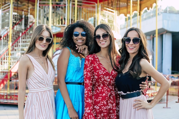 Four attractive women are posing on the urban background, hugging each otherÃ¢ÂÂs waists, smiling broadly and enjoying their youth