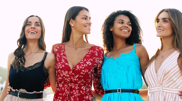 Quattro donne attraenti posano sullo sfondo urbano, si abbracciano la vita, sorridono ampiamente e si godono la loro giovinezza