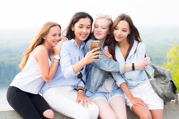 Quattro belle giovani donne che utilizzano smartphone e sorridono nel parco, all'aperto. studentesse allegre sullo sfondo della natura