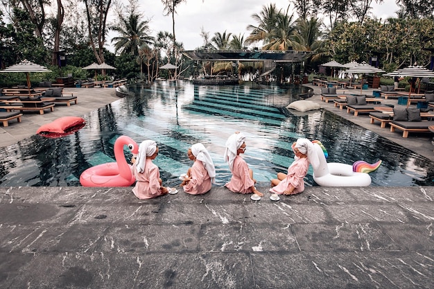 Four best friends are having fun by the pool next to the hotel. Four adorable lovely girls wearing the same clothes are posing. Back view