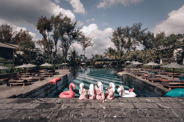 Quattro migliori amici si divertono a bordo piscina accanto all'hotel. quattro giovani donne sexy che indossano gli stessi vestiti stanno posando. vista posteriore