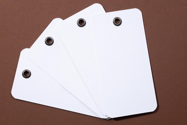 Four blank tags made of white cardboard of rectangle shape with tiny holes in upper part for clothes put in center on each other looking like fan on brown background Tag mock up Copy space