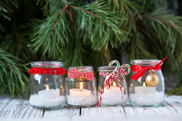 Four candles in glass jars with fir on holiday background Cozy handmade holiday home decor glass jar with candle decorated with red ribbon Christmas decorations