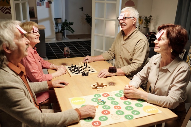 Four cheerful aged friends with notepapers on their foreheads sitting by table