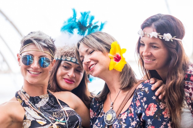 Четыре веселые красивые молодые женщины празднуют вместе и делают селфи, улыбаясь и веселясь в концепции вечеринки дружбы с цветным платьем и цветами, толпятся на ярком фоне, люди счастливы
