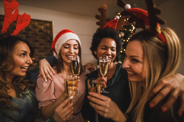 Photo four cheerful multietnic girls toasting with champagne on christmas or new year's home party.