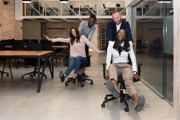 Photo four cheerful young multiracial entrepreneurs having fun while running around in office chairs and smiling