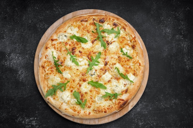 Four cheese pizza quattro fromaggi with arugula leaves on a wooden board on gray concrete Top view