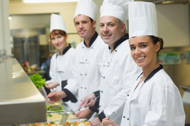 Four chefs smiling at camera while working at serving trays