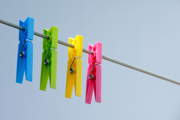 Four colorful clothespins yellow green blue and pink hanging on the clothesline