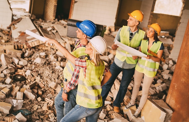 Four construction architects review plans of building damaged in the disaster. Pointing at damages.