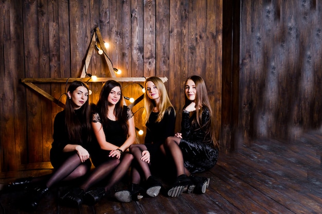 Four cute friends girls wear black dresses against large light christmas star decoration on wood wall