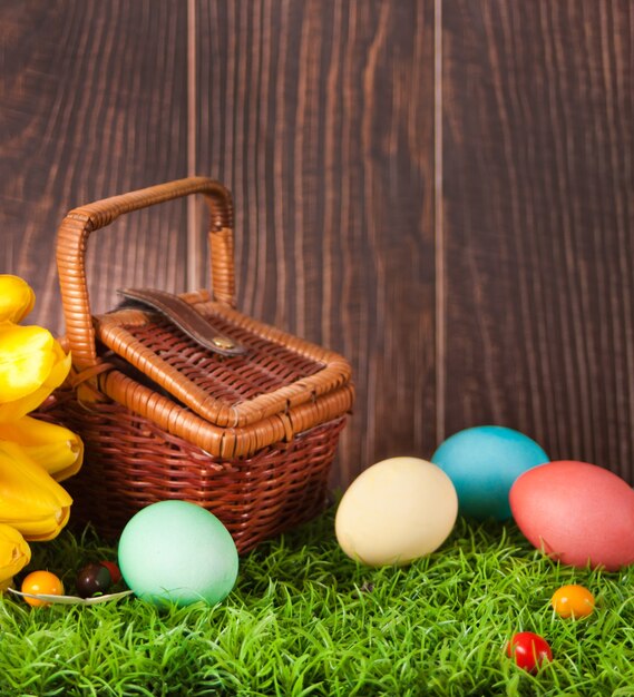 Four decorated colorful Easter eggs in the grass with flowers tulips and picnic basket.