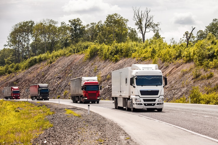 Photo four different coloured trucks moving by a road