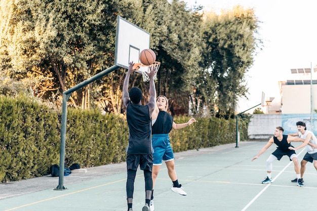 Four diverse people playing basketball in a public outdoor\
court