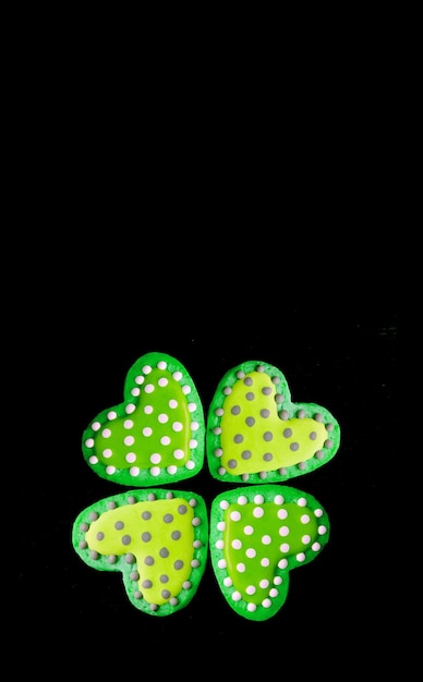 Four of dotted heart shaped royal icing cookies in fourleaf clover form on black backdrop