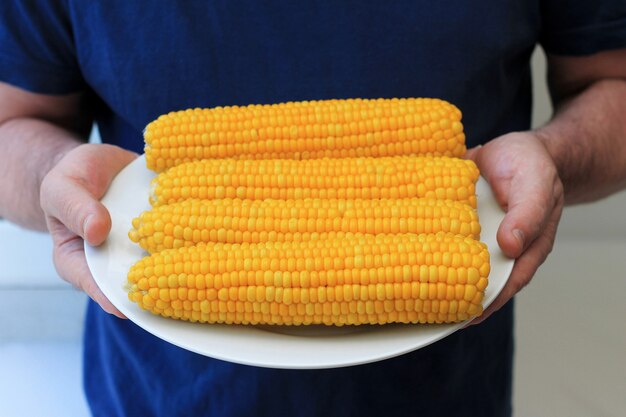 Four ears of boiled corn on a plate in male hands. 