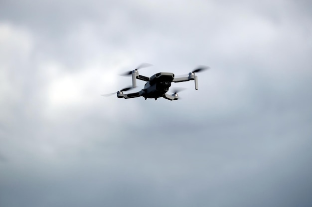 Four engine drone with camera is flying in the grey stormy cloudy sky front view close up