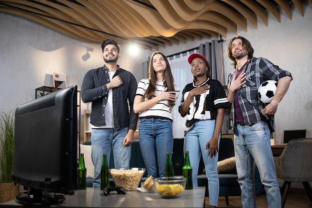 Four fans singing hymn before watching football game on TV