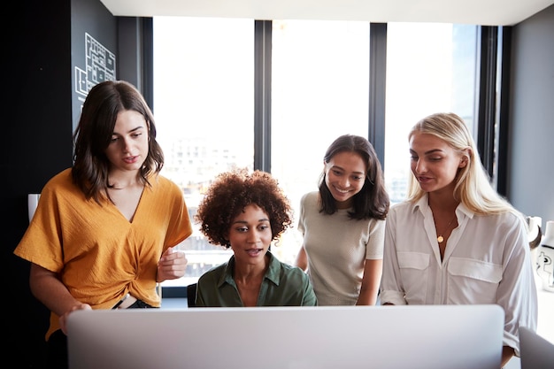 Four female creatives working around a computer monitor in an office front view close up