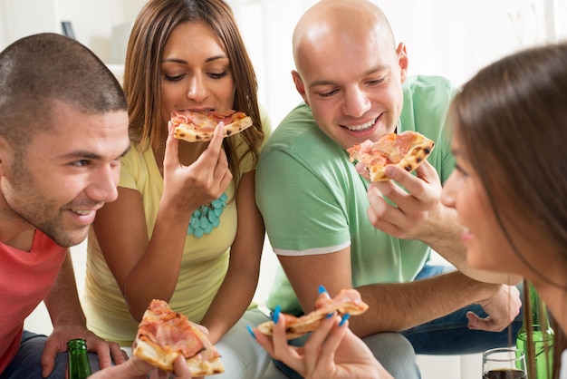 Four friends enjoying to eating pizza together at home party.