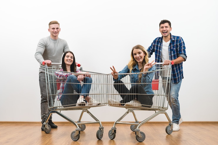 Photo the four friends fun with a shopping cart on a white wall background