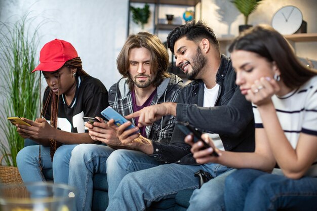 Photo four friends relaxing on couch with gadgets in hands