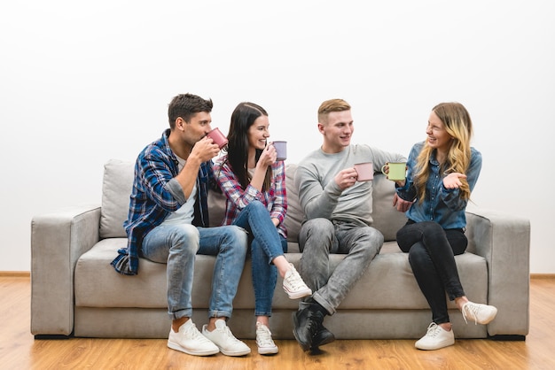 The four friends with cups sit on the sofa on a white wall background