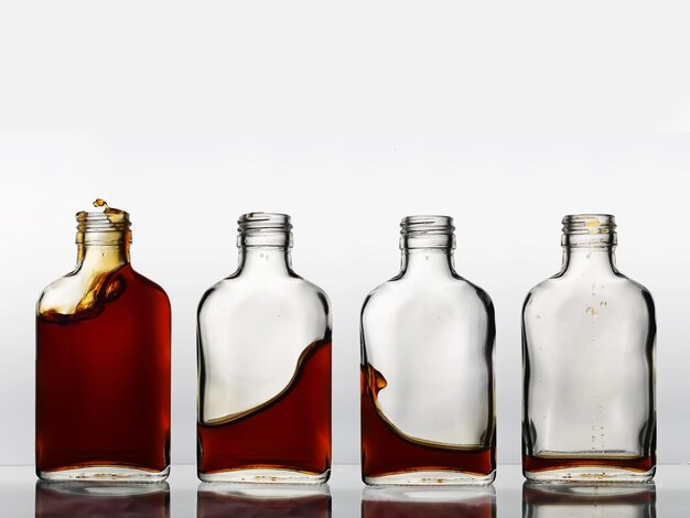 Photo four glass bottles in a row with different amount of brown color beverage cognac