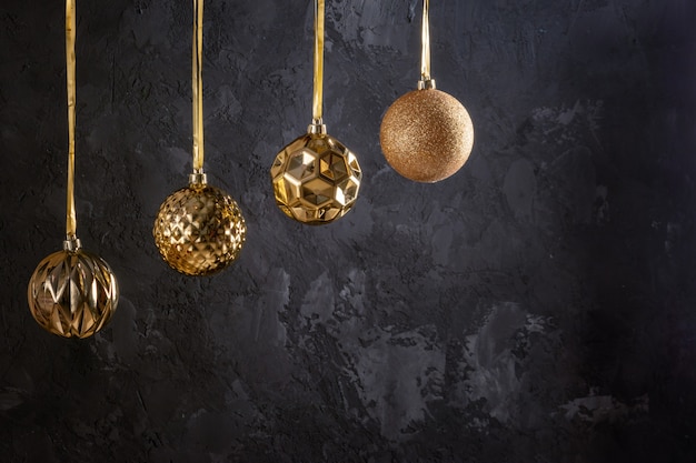 Four golden Christmas balls hanging on ribbons. Near the copy space on a black textured background. Beautiful festive layout.