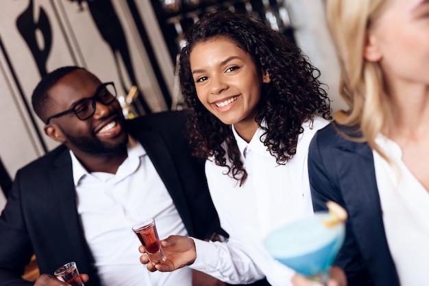 Four guys and girls are drinking cocktails in a bar.